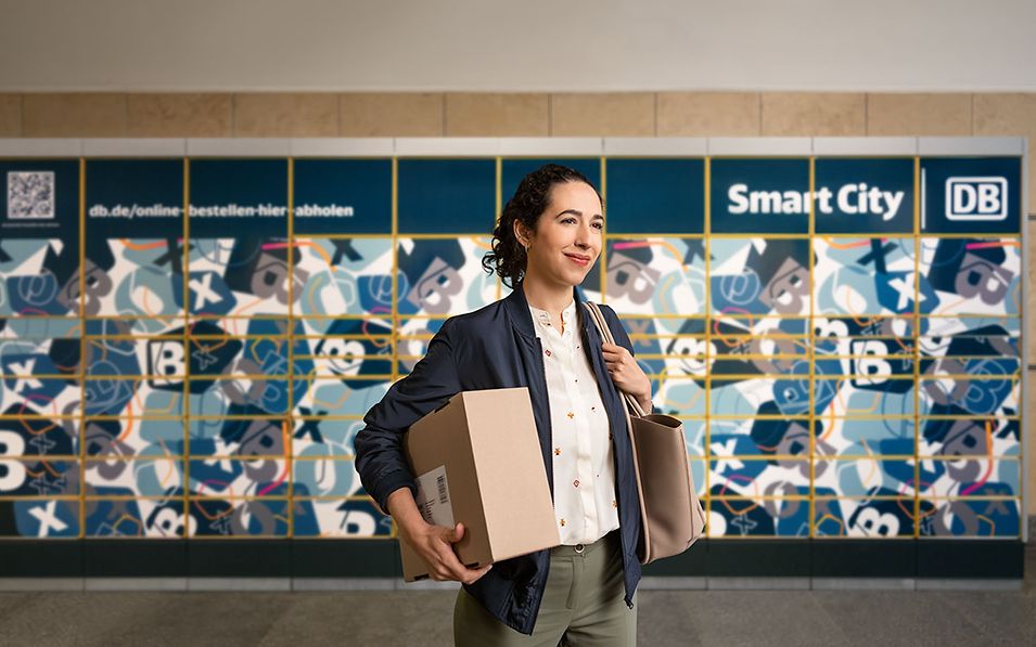 Frau trägt ein Paket und steht vor einer Abholstation